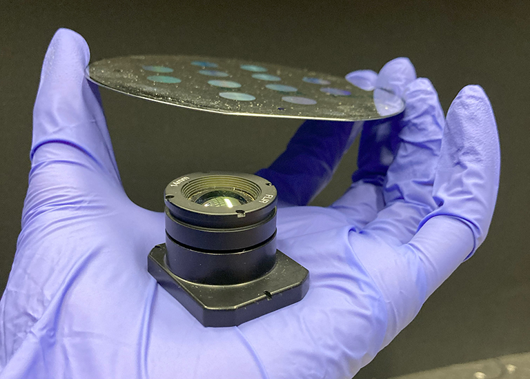 side view of a fabricated wafer containing meta-optics held above a conventional refractive lens.