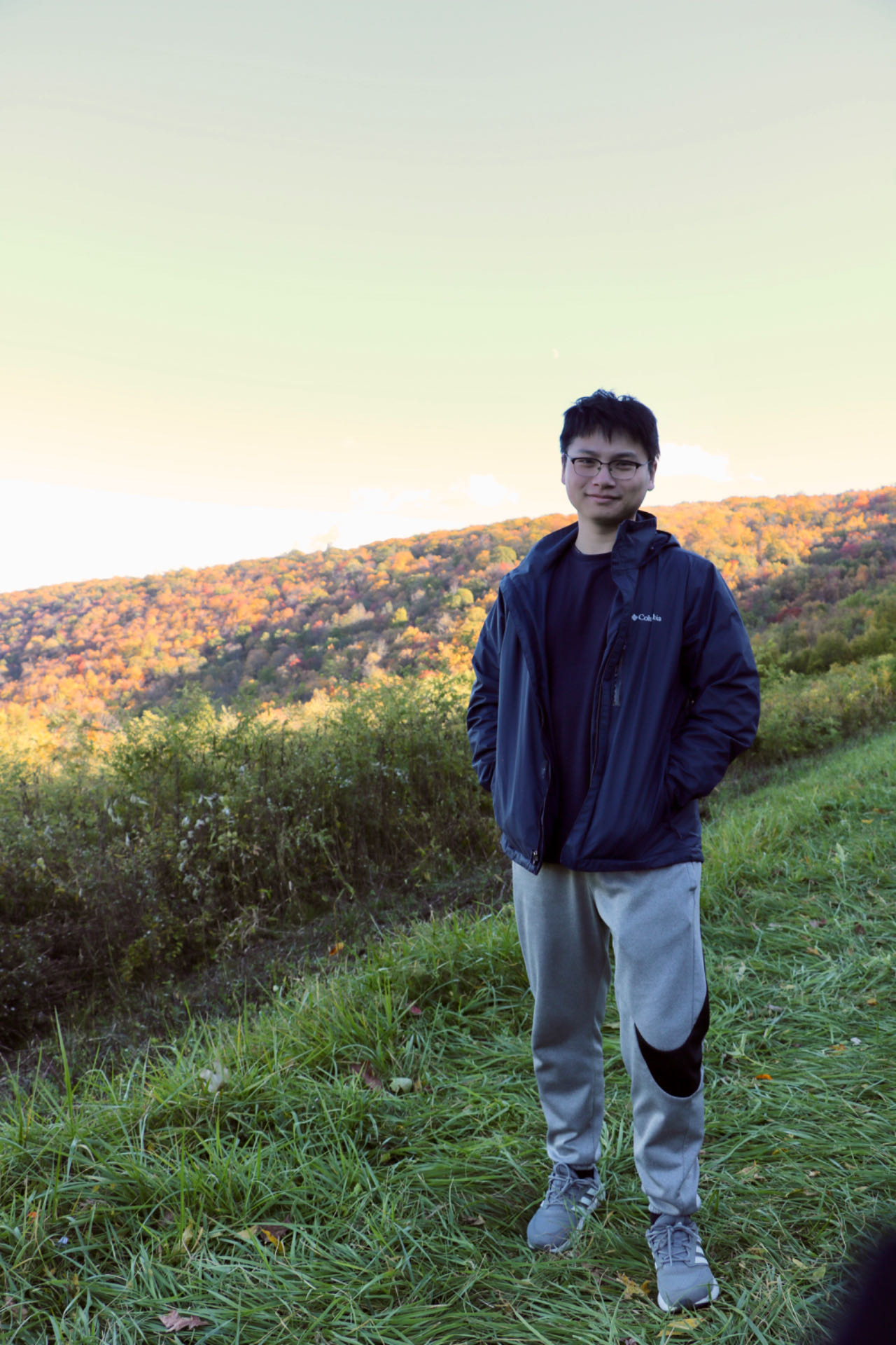 Rui Chen standing on green grace with mountains in the background.